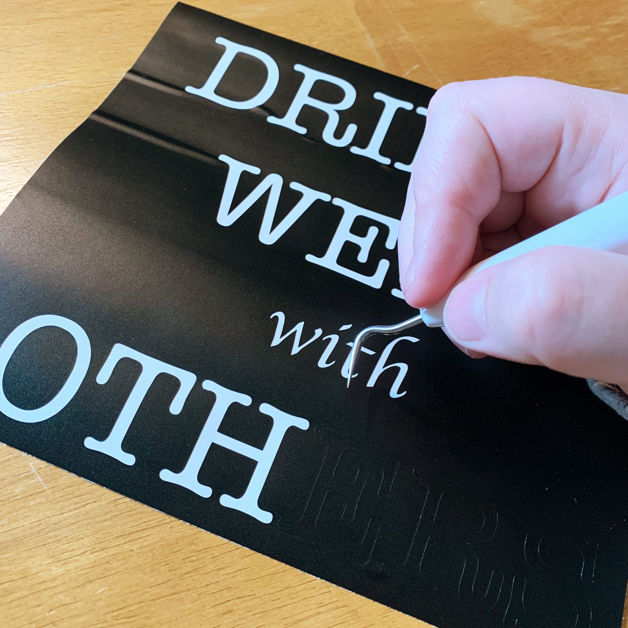 A hand using a tool to weed vinyl from a sheet of black vinyl.