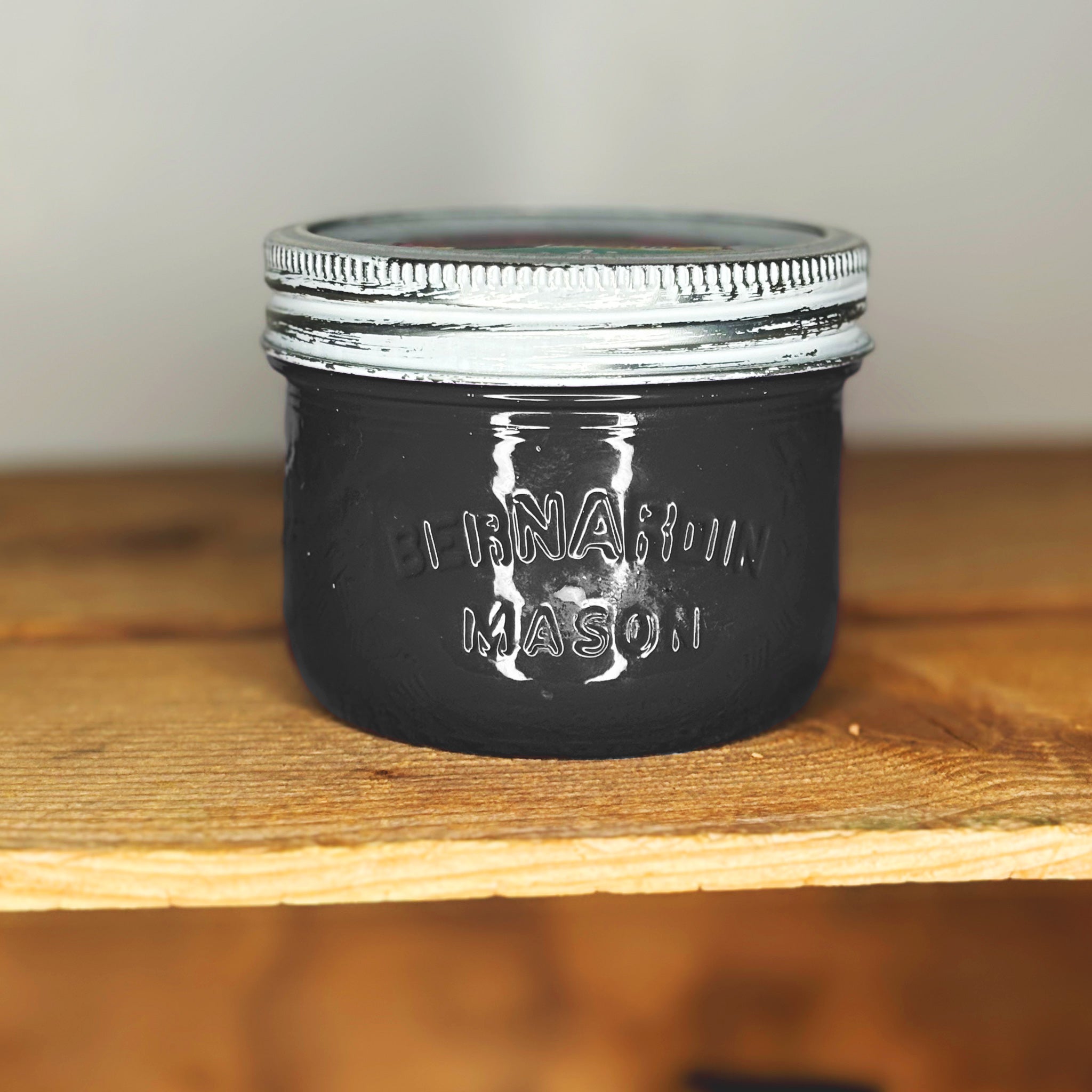 A black mason jar with silver lid on a wooden surface.