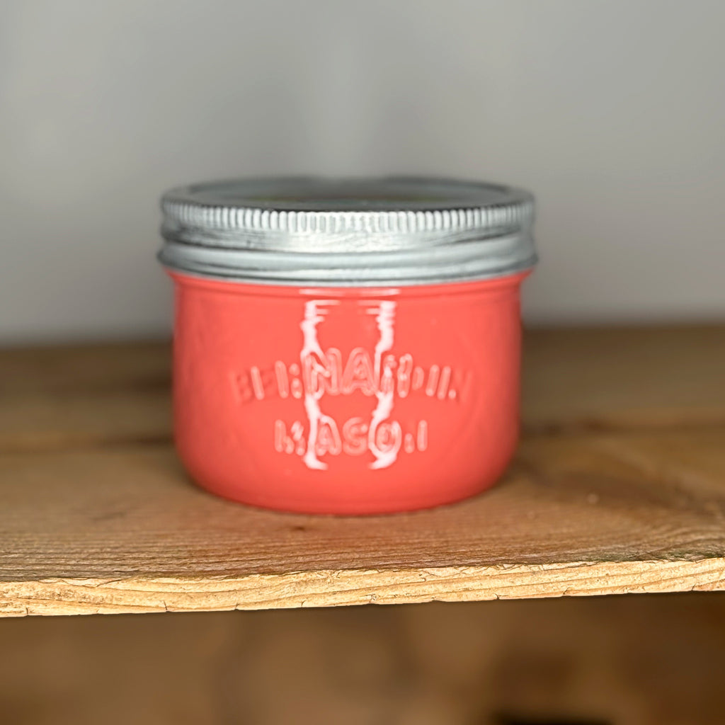 Coral mason jar with silver lid on a wooden surface.