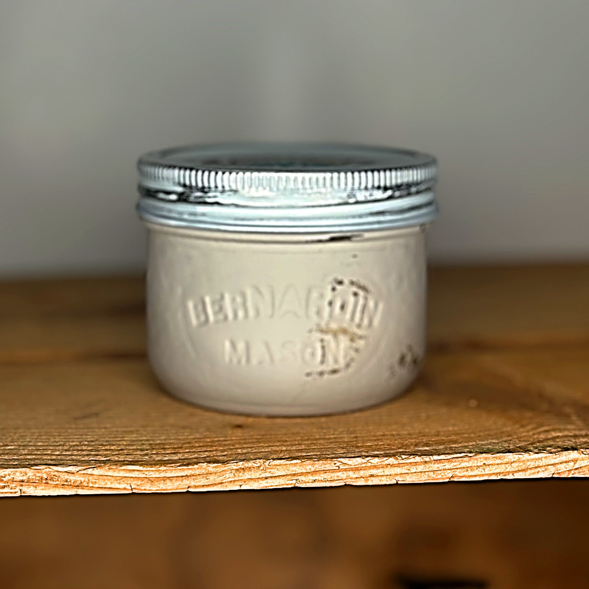 A fawn coloured mason jar with a silver lid on a wooden surface.