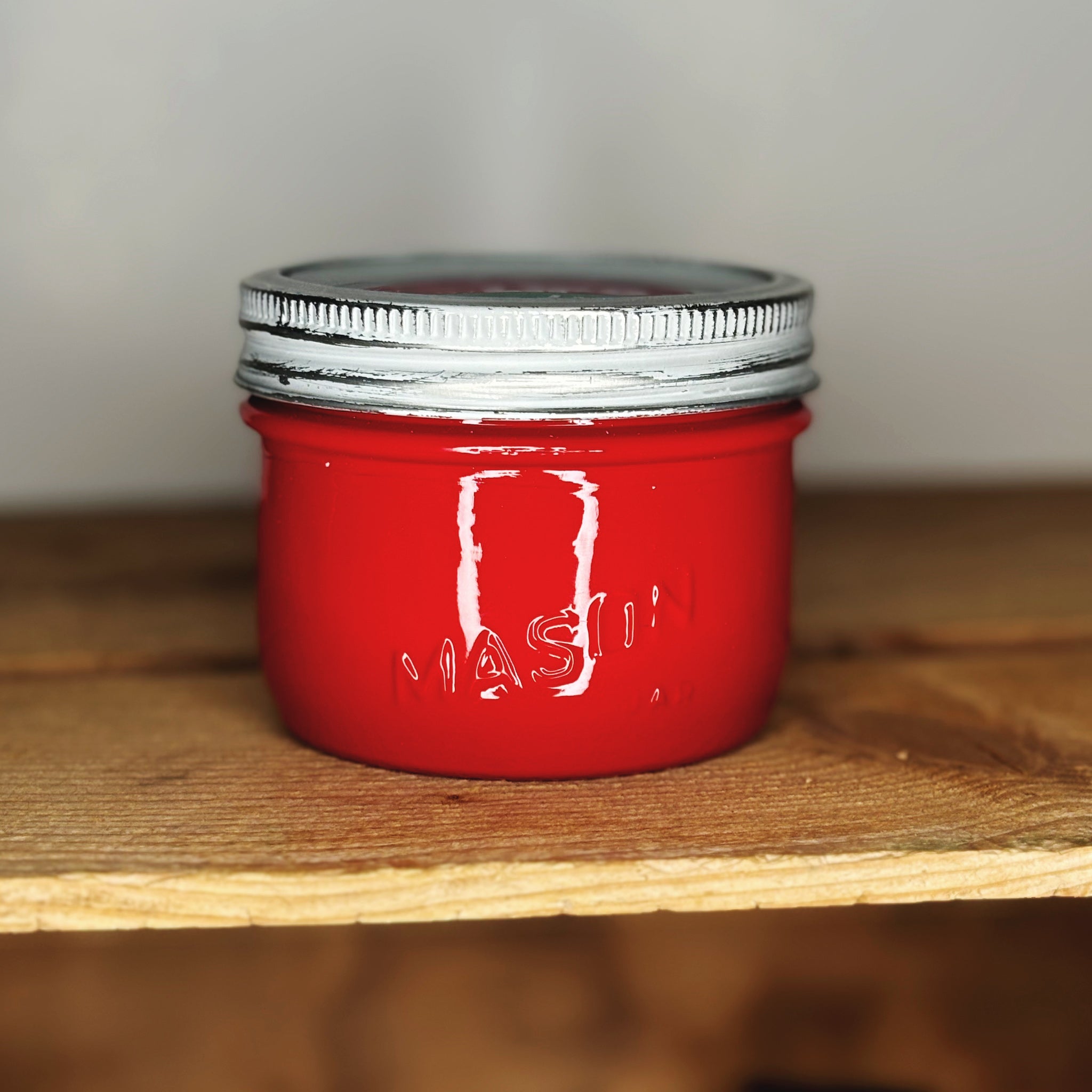 Red jar with silver lid on a wooden surface.