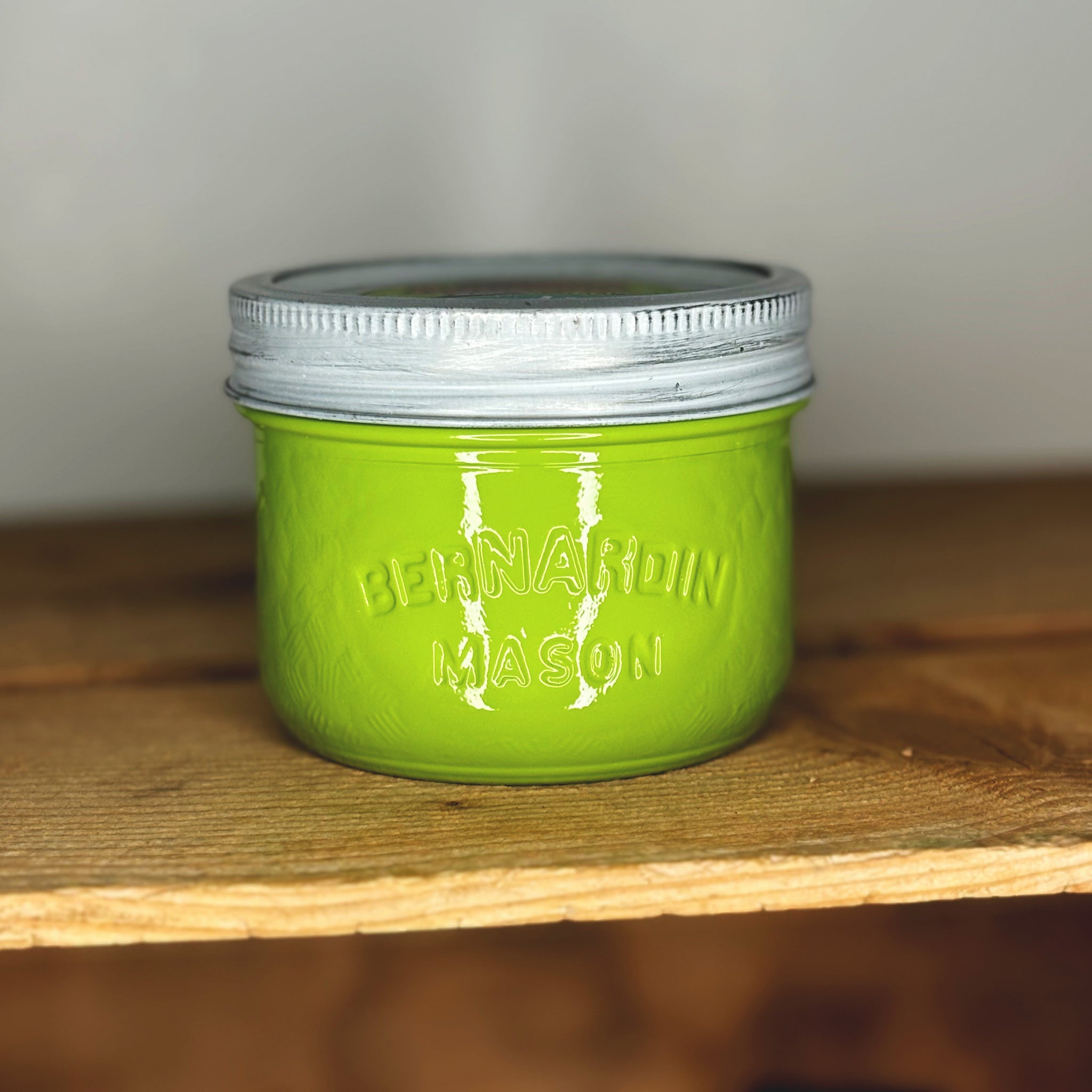 Green mason jar with silver lid on a wooden surface.