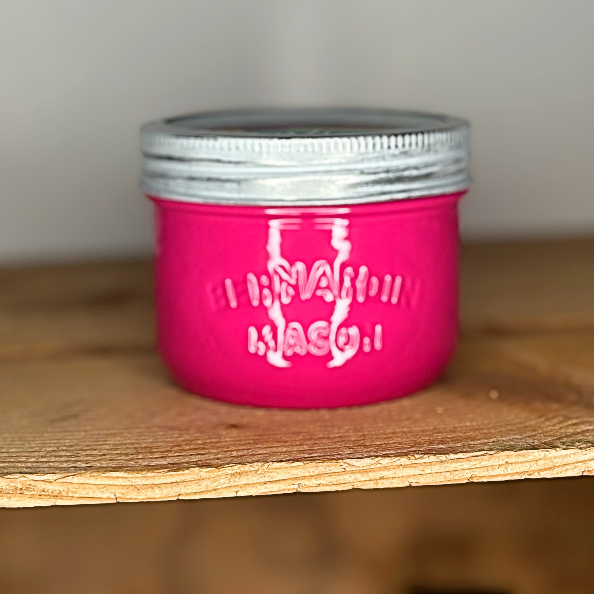 Pink mason jar with silver lid on a wooden surface.