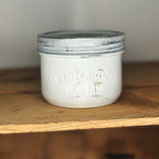 White jar with a metal lid on a wooden shelf.