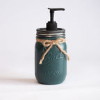 A green mason jar soap dispenser with a pump and twine on a light background.