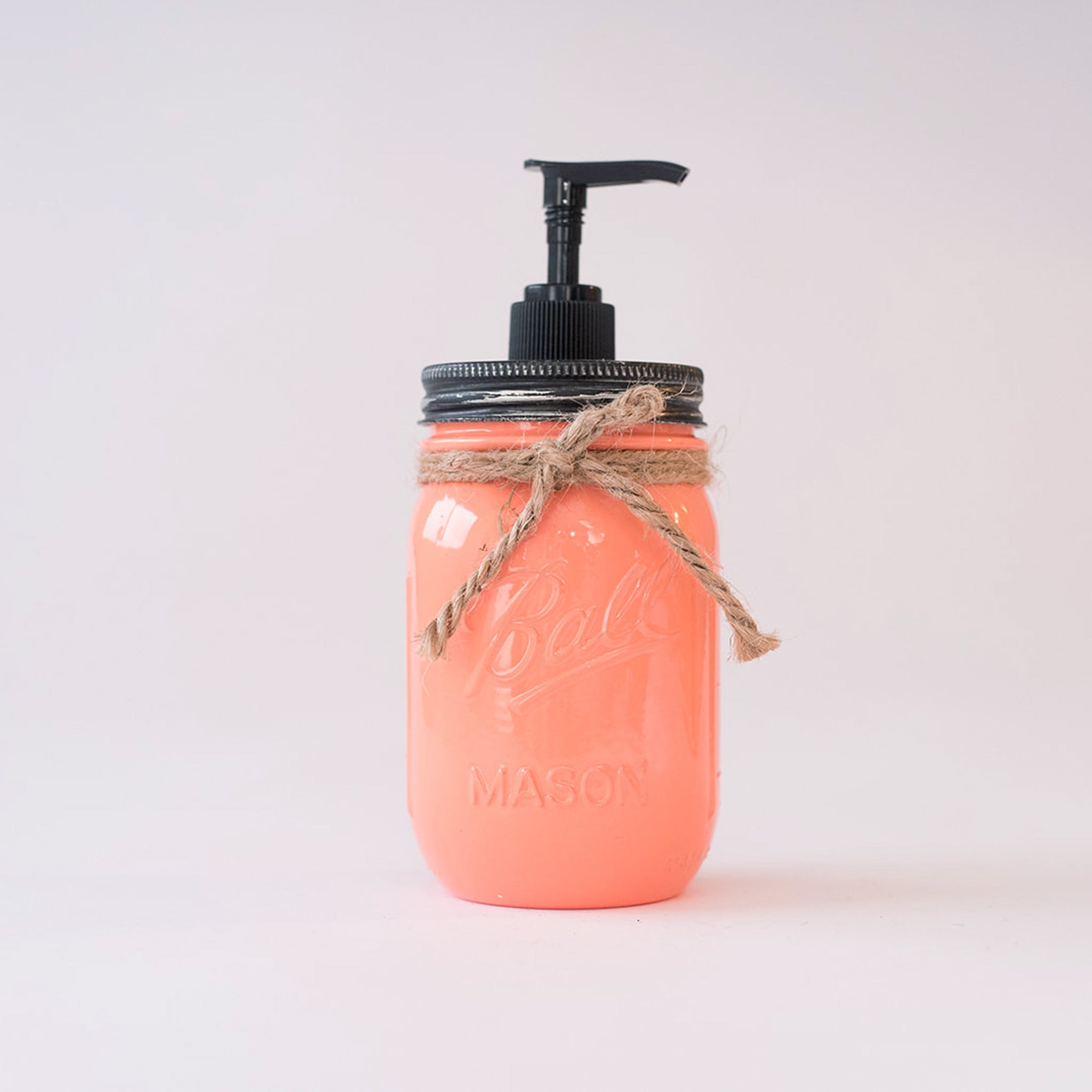 A coral-colored mason jar soap dispenser with a black pump on a white background.