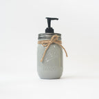 A grey mason jar soap dispenser with a pump and twine on a white background.