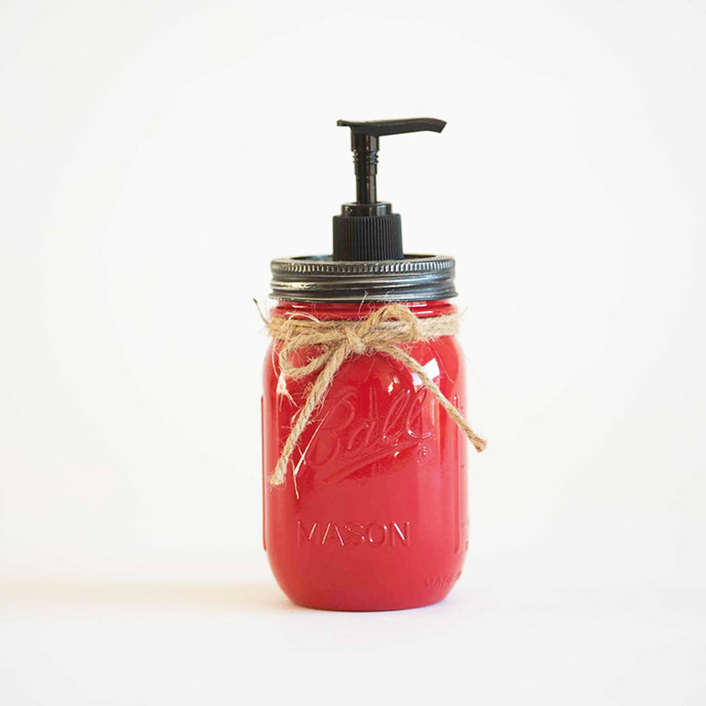 A red mason jar soap dispenser with a black pump and twine bow on a white background.