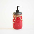 A red mason jar soap dispenser with a black pump and twine bow on a white background.