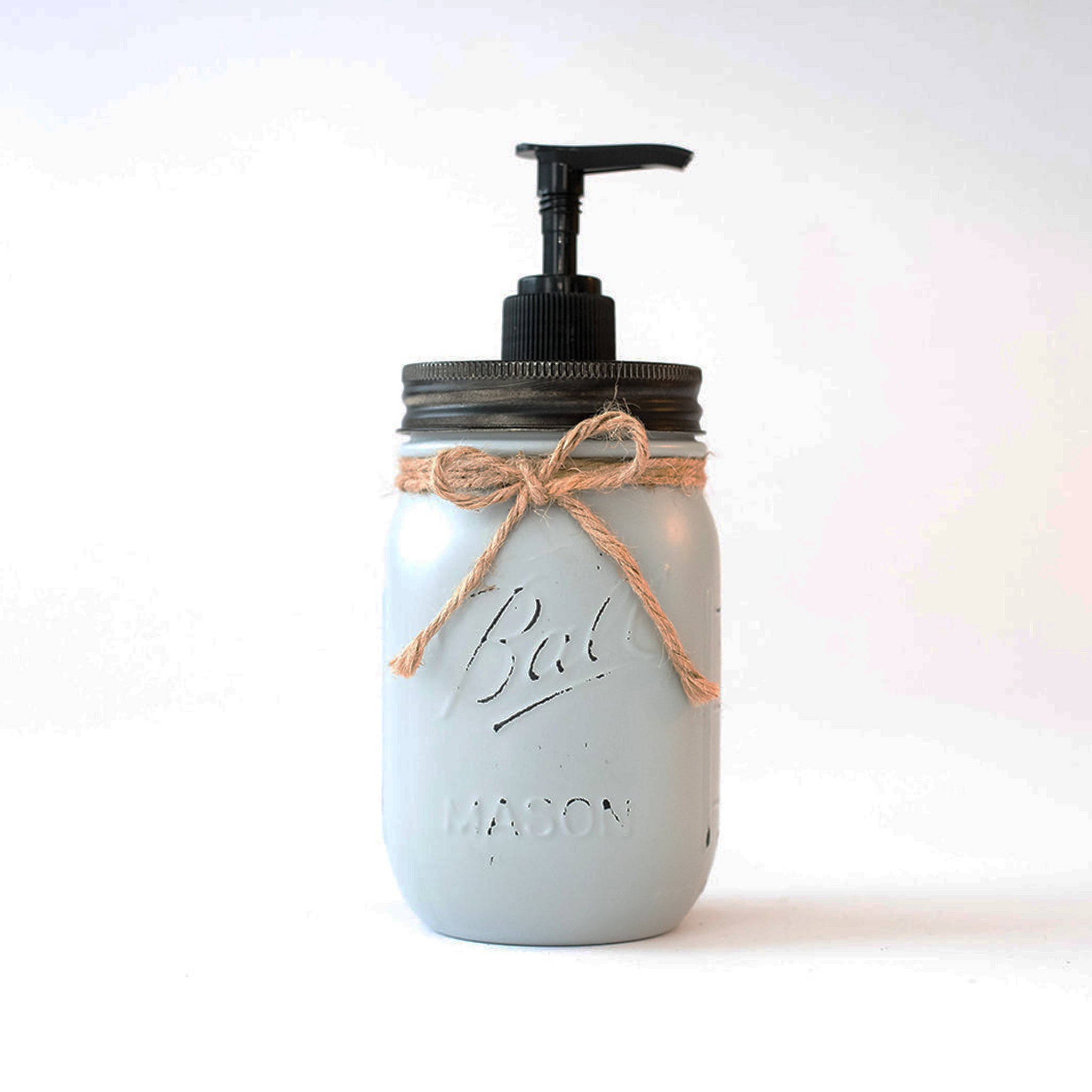 A mason jar soap dispenser with a pump and twine on a white background.