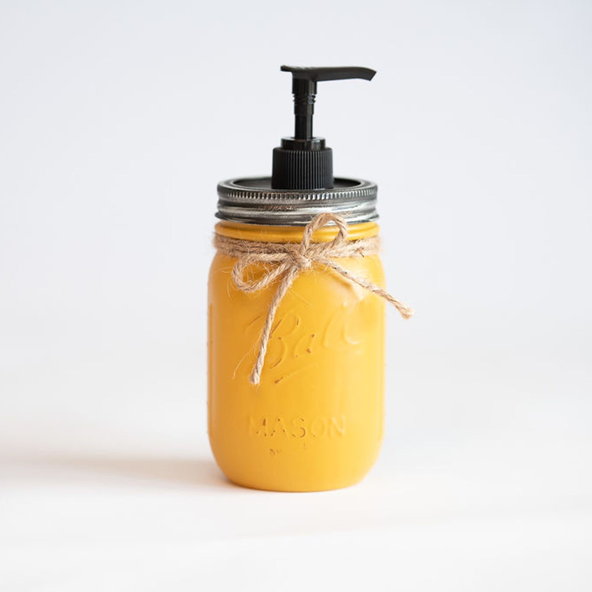 A yellow mason jar soap dispenser with a black pump on a white background.