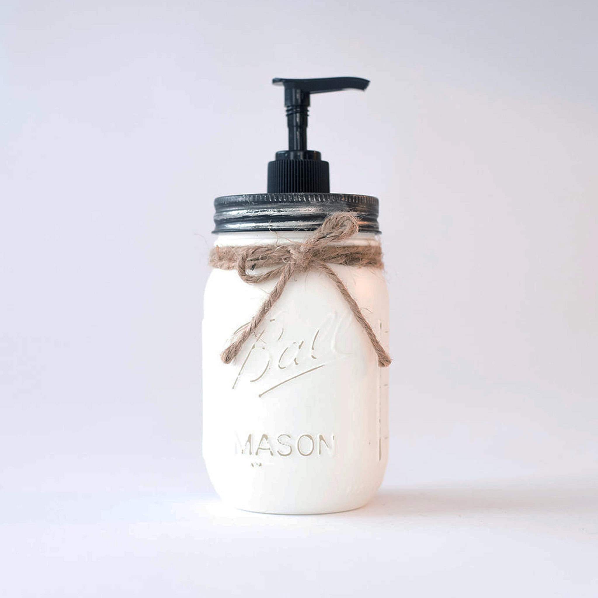 A white mason jar soap dispenser with black pump and twine bow on a white background