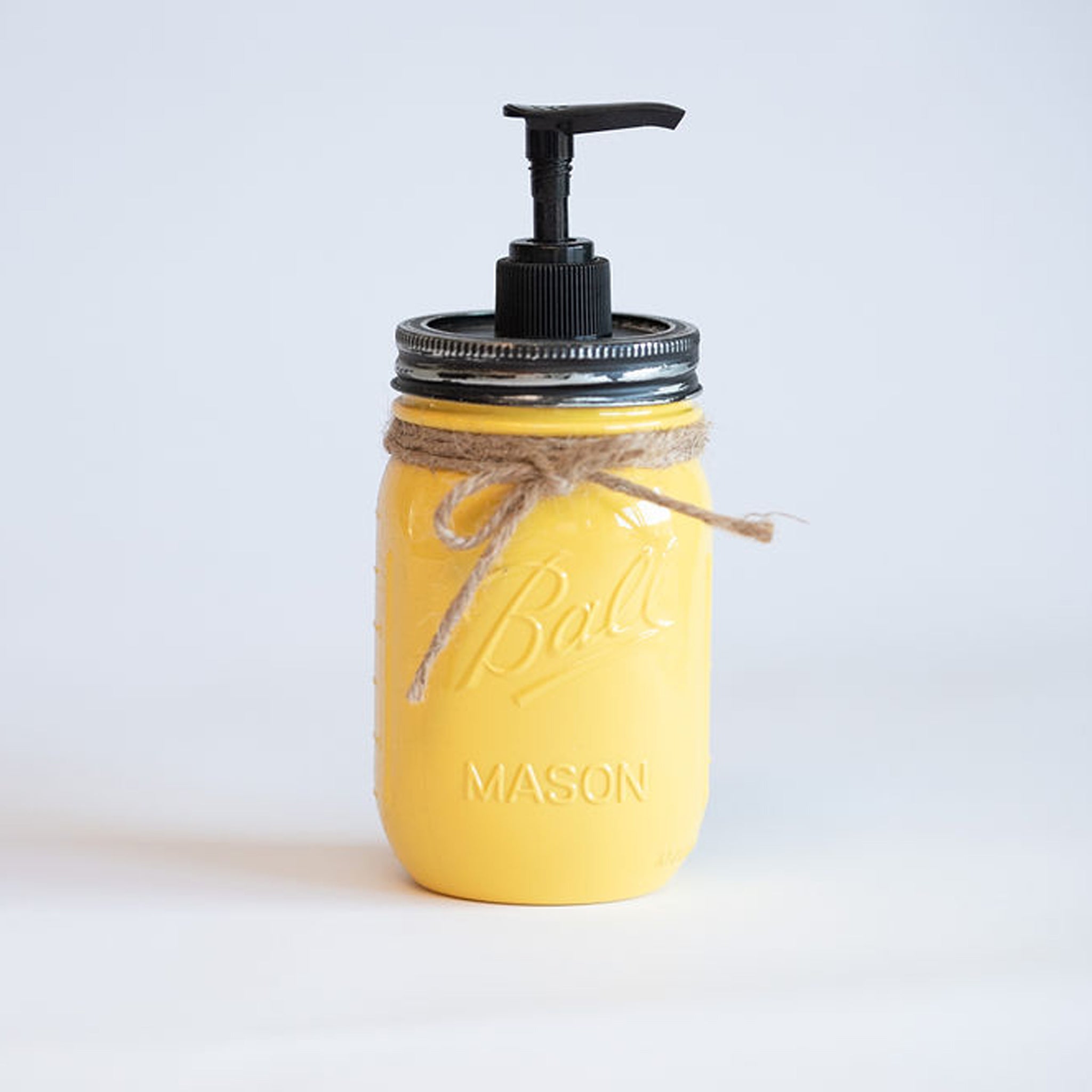 A yellow mason jar soap dispenser with a black pump on a white background.