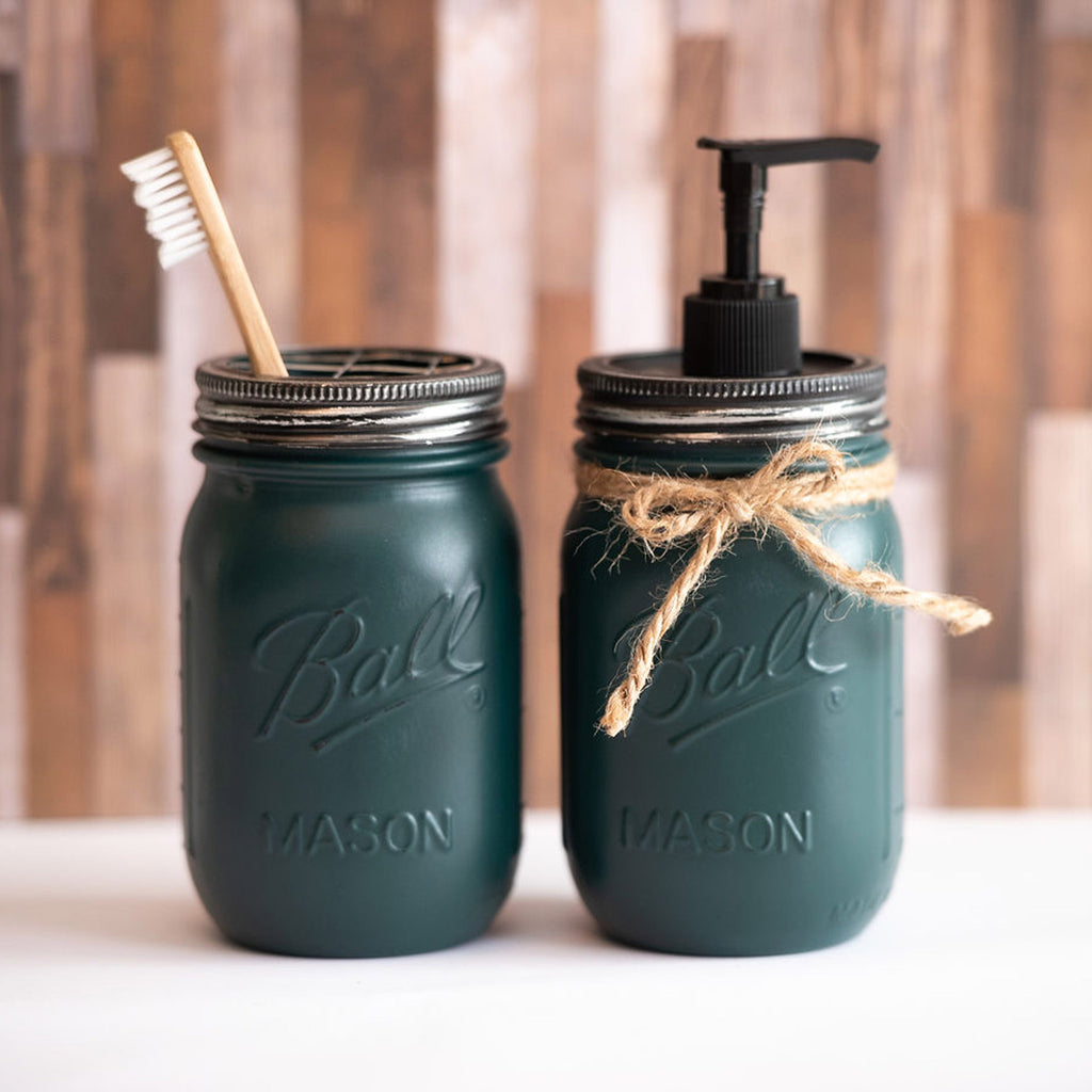 Two green mason jar bathroom sets with a toothbrush and pump dispenser on a wooden surface.