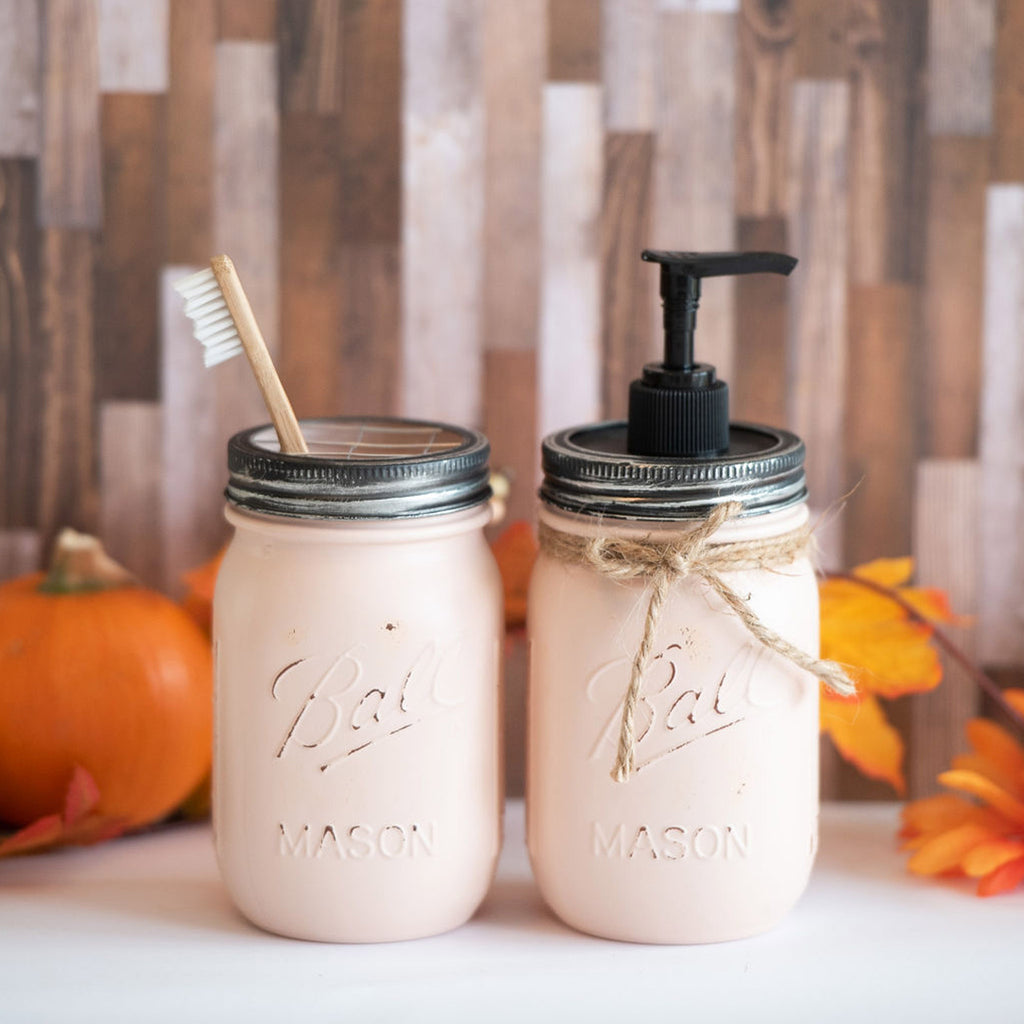 Two mason jars with pump soap dispenser and toothbrush, decorated for autumn, on a wooden surface.