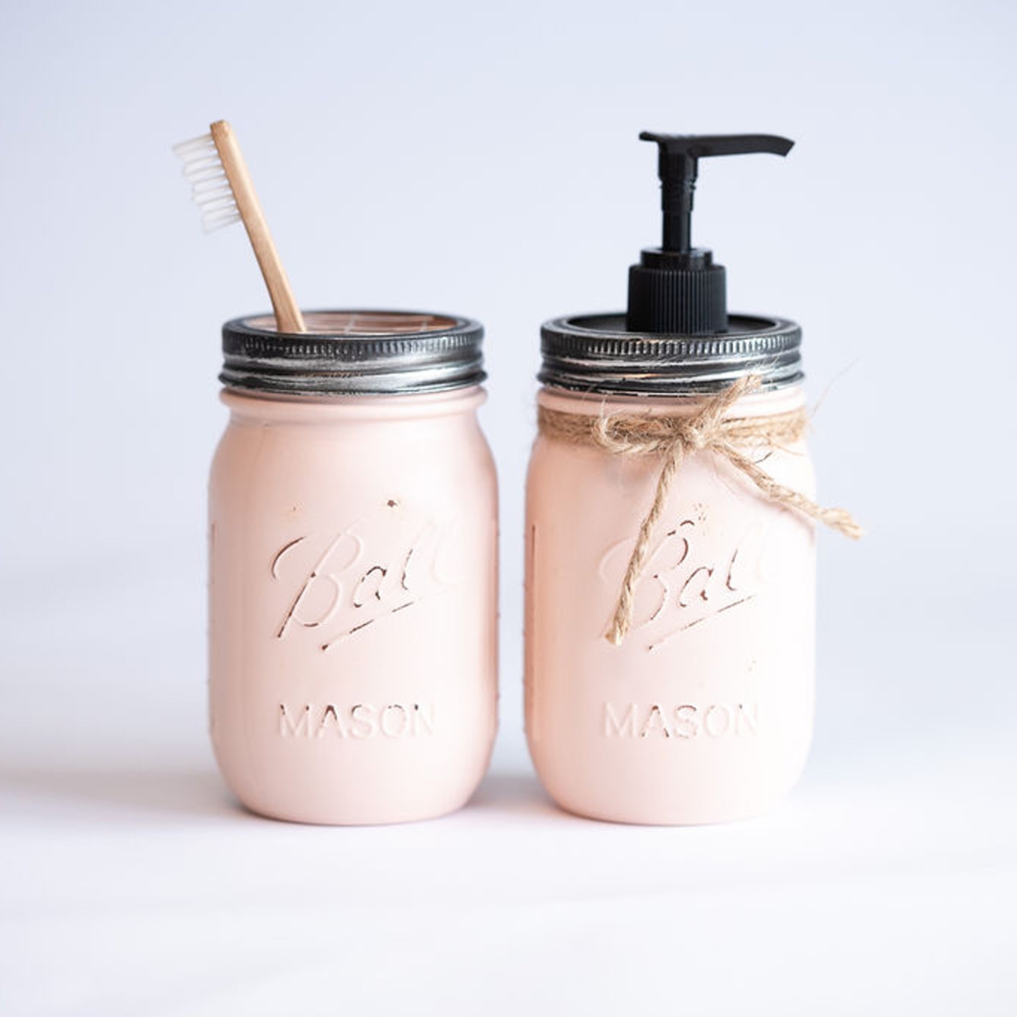 Two pink mason jars with a straw and pump on a light gray background.