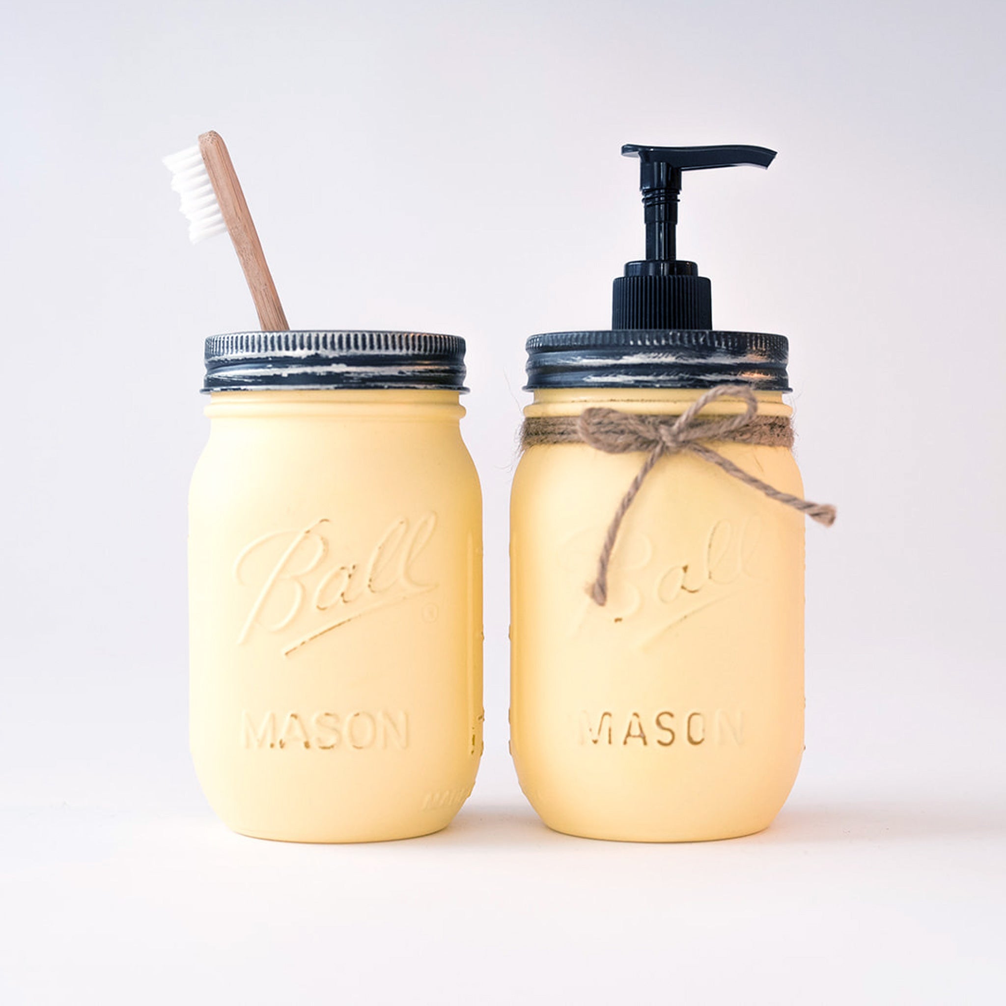 Two yellow mason jars, one with a toothbrush and the other with a pump dispenser on a white background.