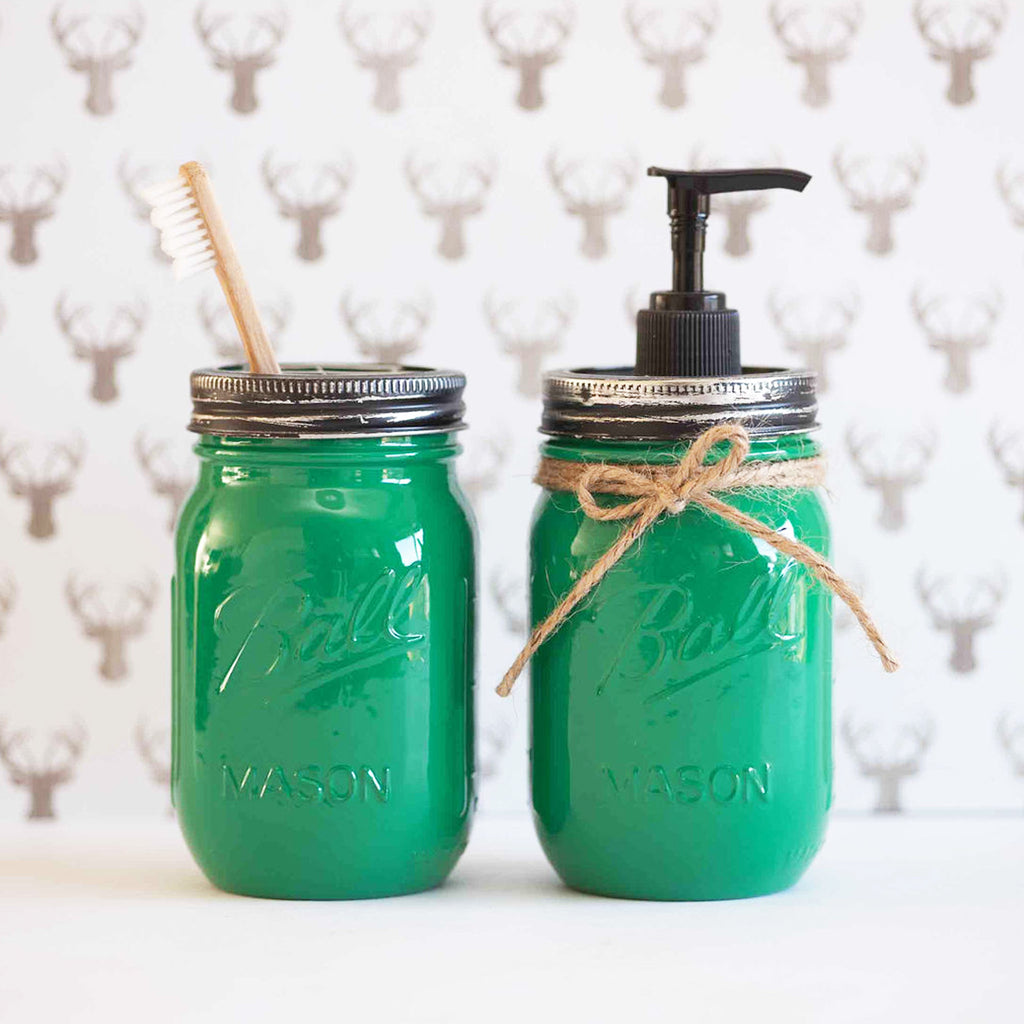 Two green mason jars, one with a toothbrush and the other with a pump dispenser, on a neutral background.