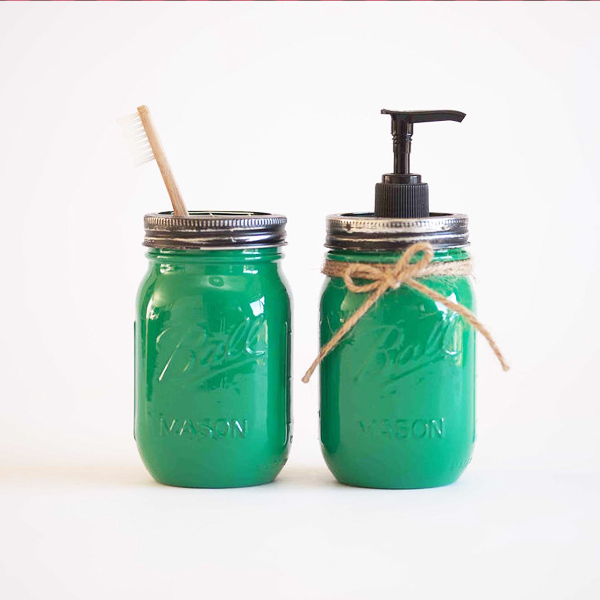 Two green mason jars, one with a straw and the other with a pump dispenser on a white background.