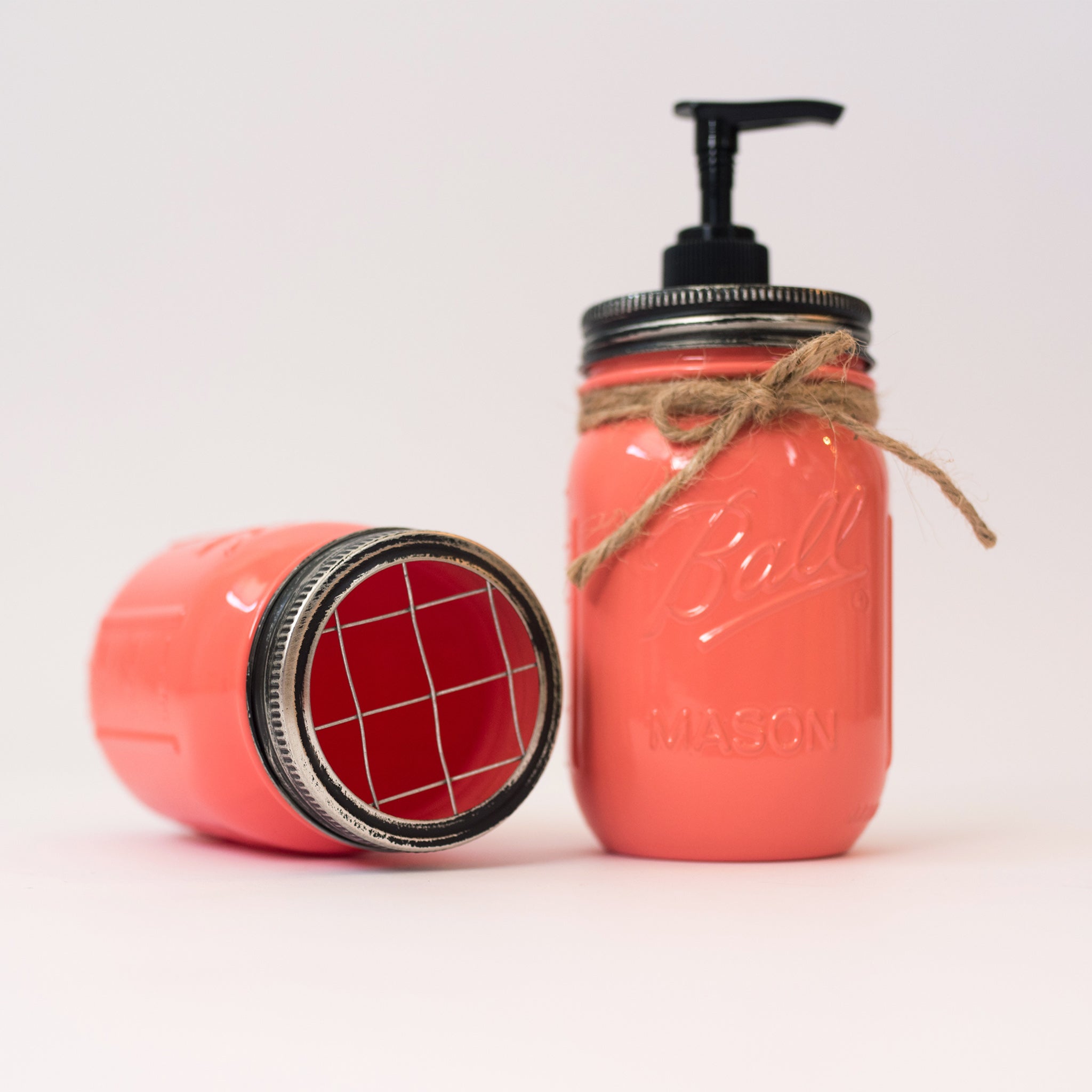 Two coral-colored mason jars with pump and lid on a white background.