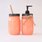 Two coral-colored mason jars with a toothbrush and pump on a light background.