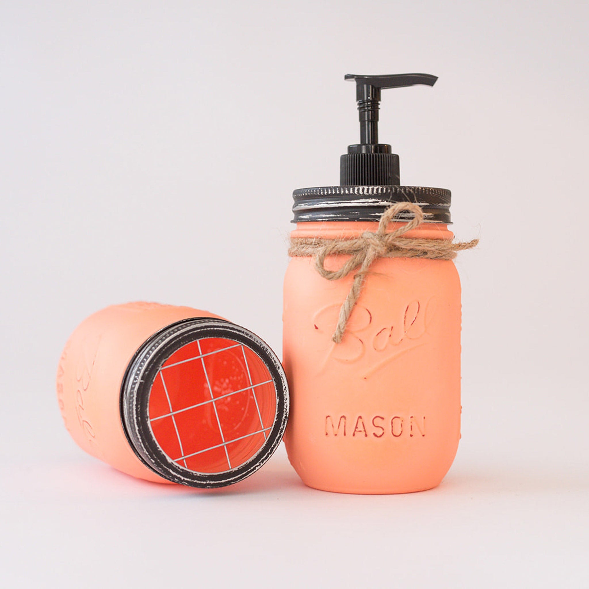 Coral-colored mason jar soap dispenser with pump on a white background.