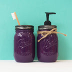 Two purple Ball jars with a toothbrush and soap dispenser on a teal background.