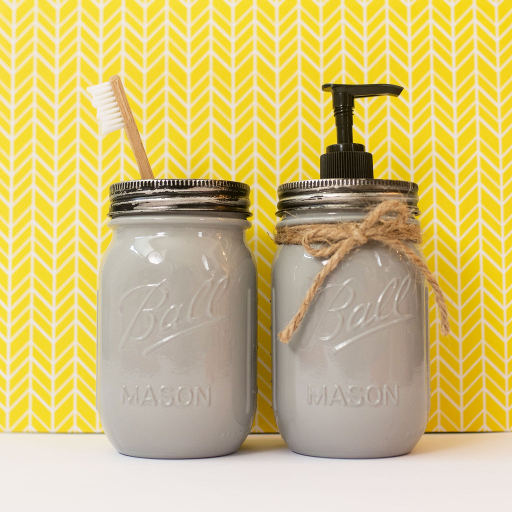 Two grey mason jars with a toothbrush and pump dispenser against a yellow patterned background.