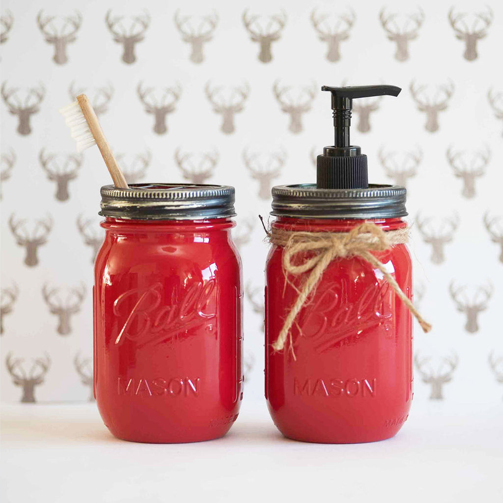 Two red mason jars with a brush and pump dispenser on a deer head pattern background.
