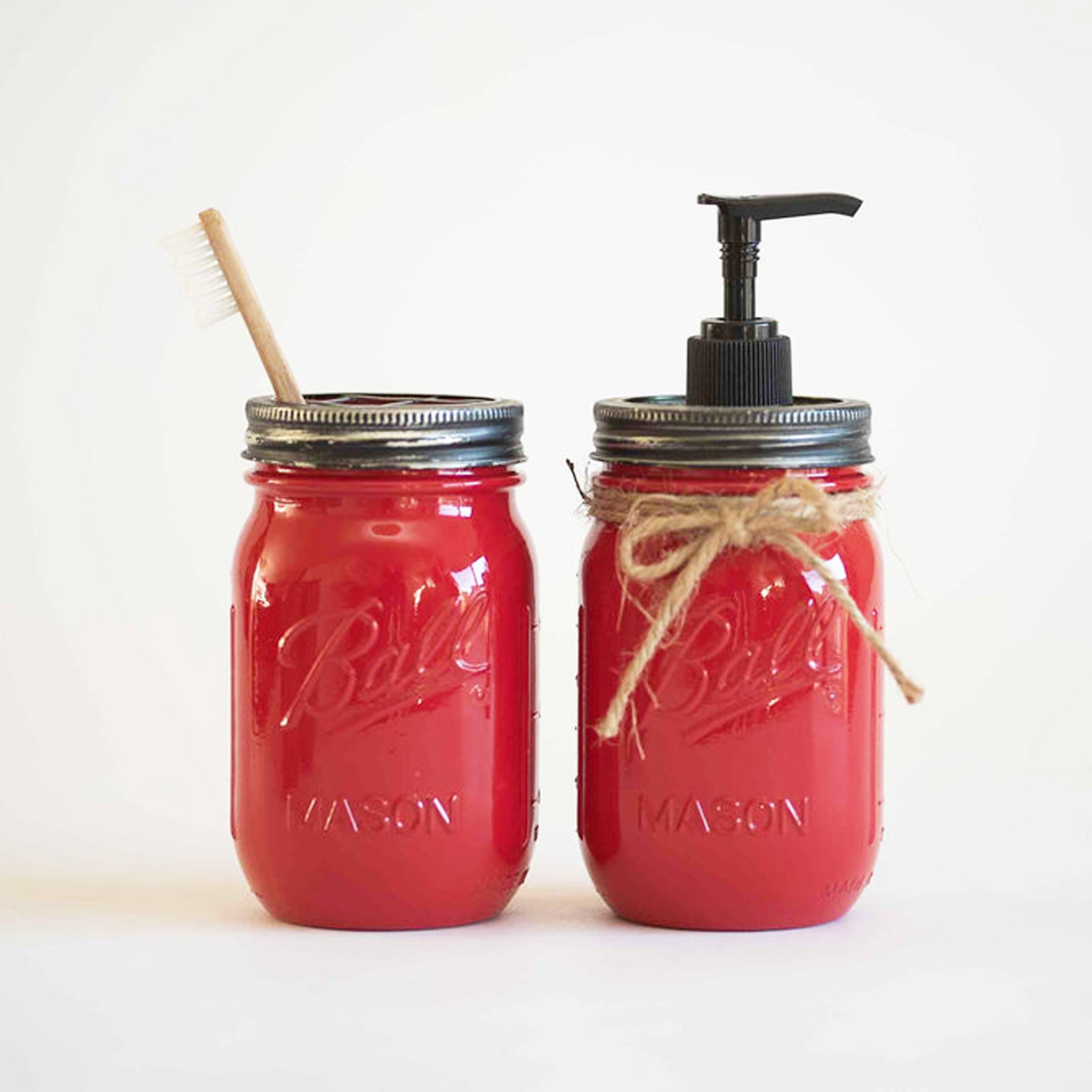 Two red mason jars, one with a toothbrush and the other with a pump dispenser on a white background.