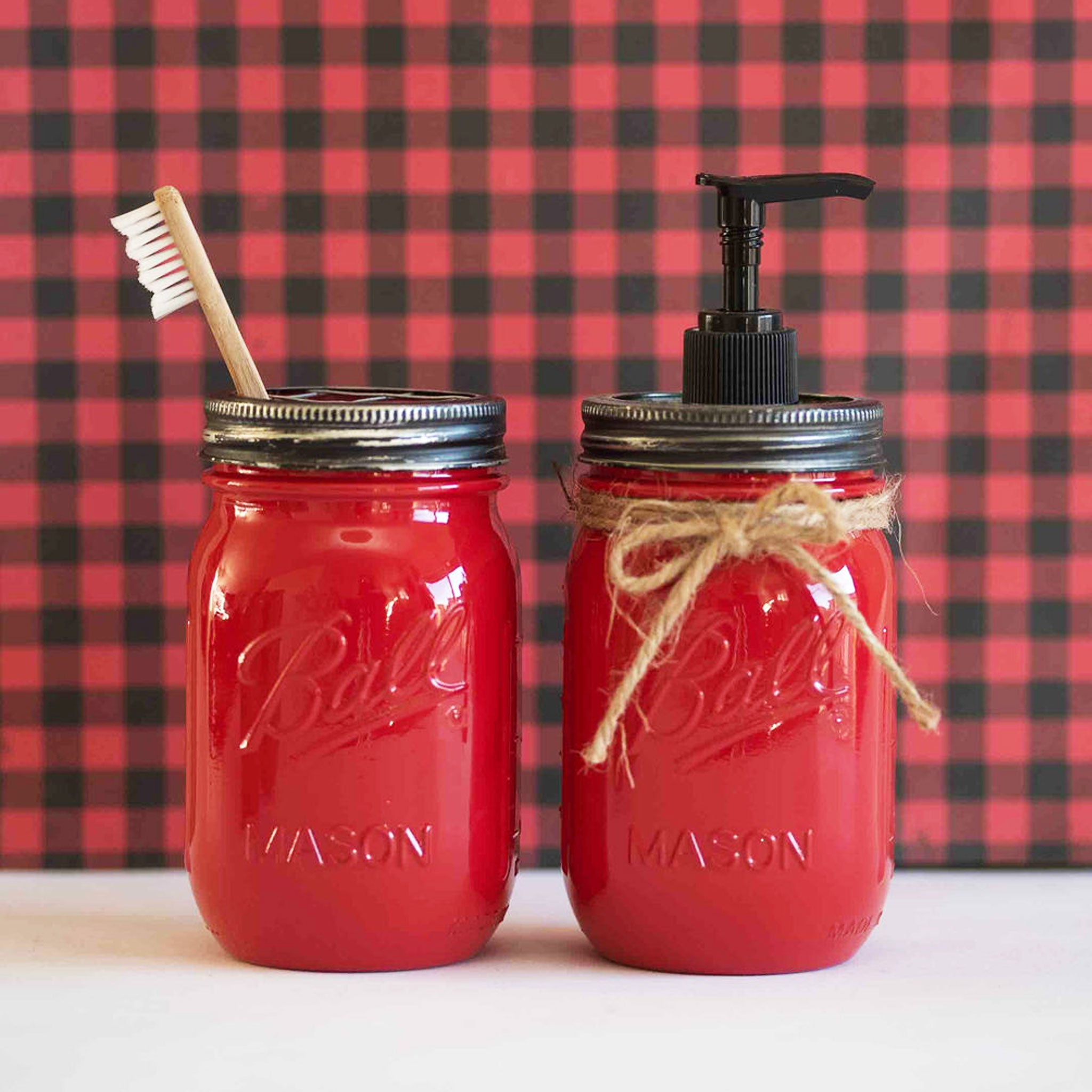 Two red mason jars with a toothbrush and pump dispenser against a red and black checkered background.