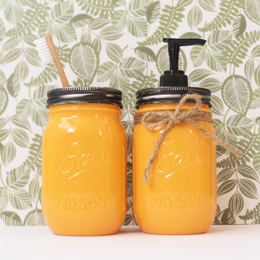 Two yellow Mason jar products with a pump and toothbrush against a leaf-patterned background.