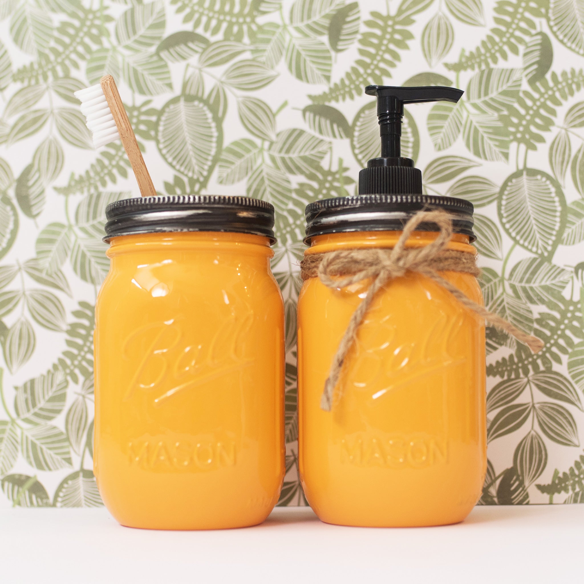 Two yellow Mason jar products with a pump and toothbrush against a leaf-patterned background.