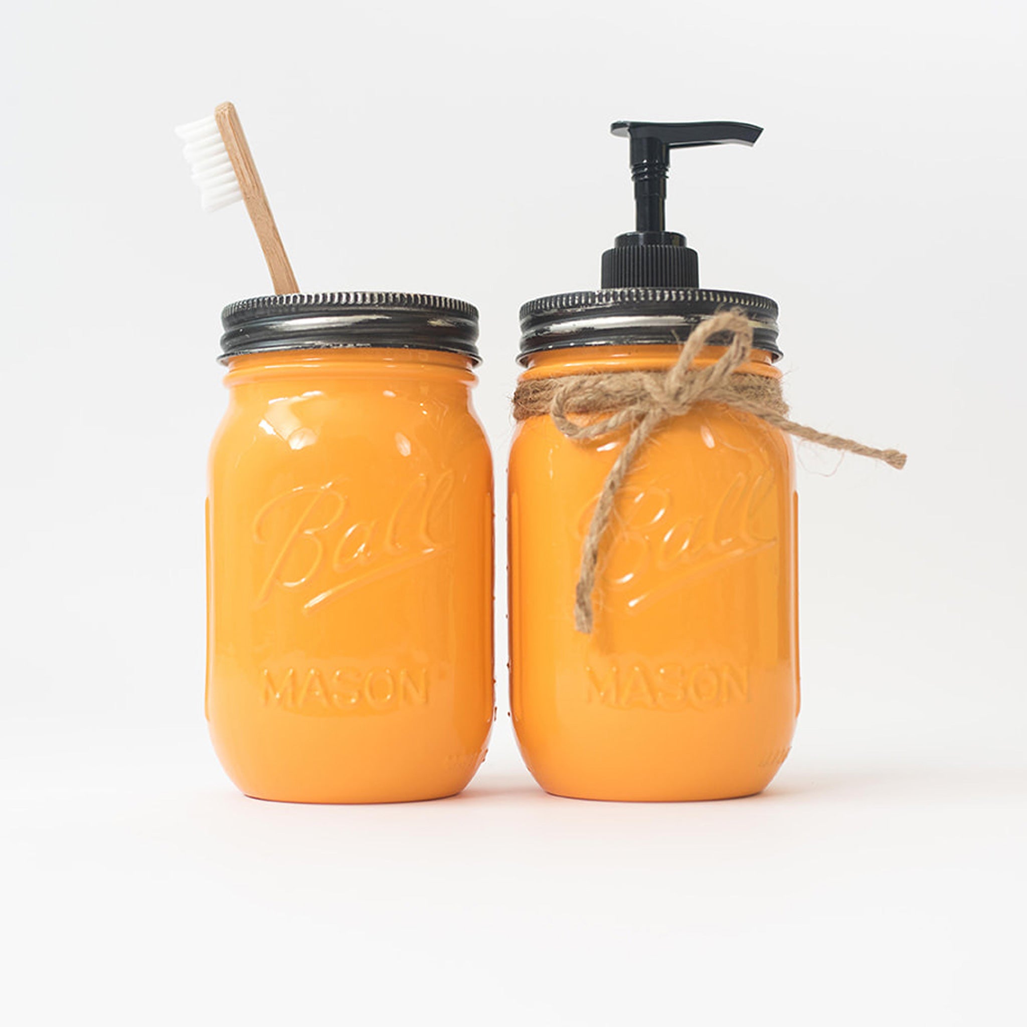 Two orange mason jars with a wooden toothbrush and pump dispenser on a white background.