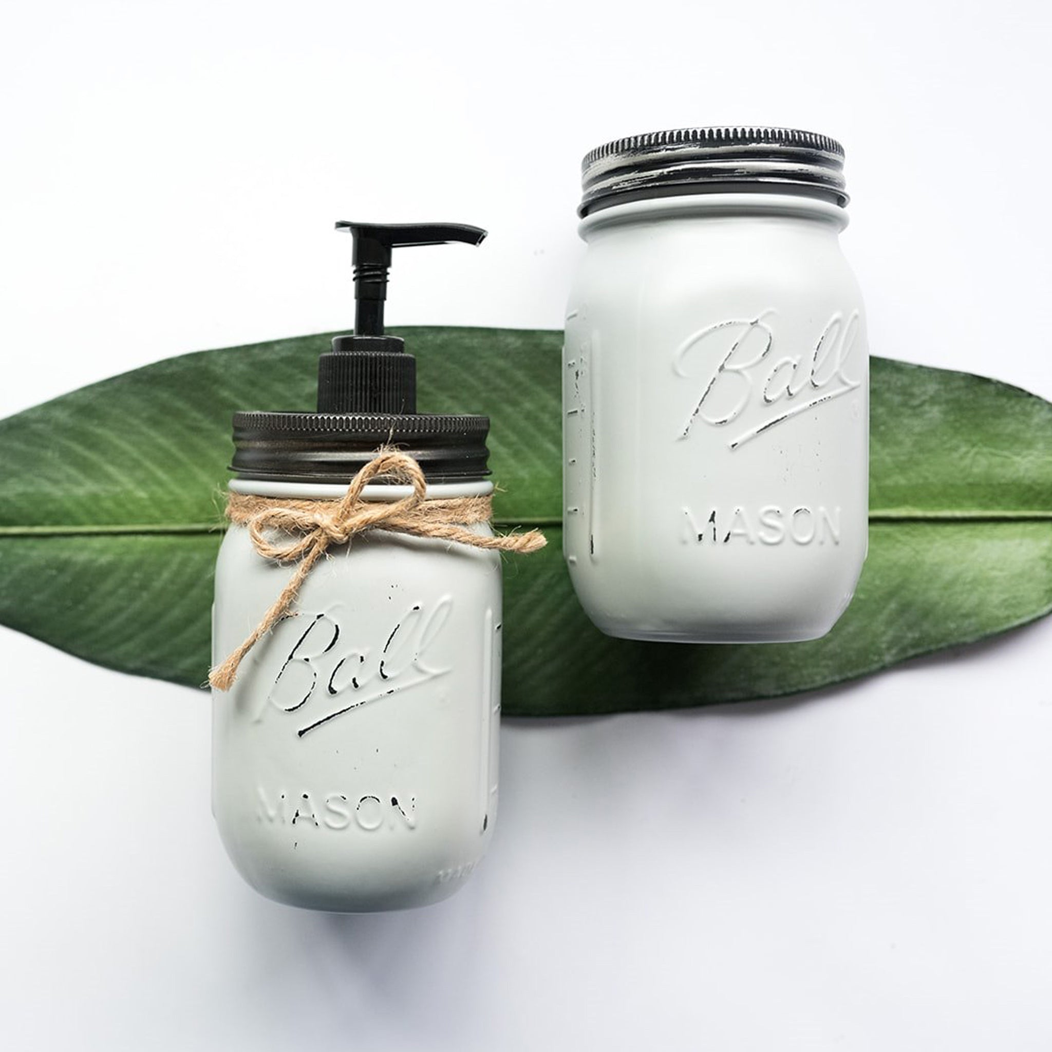 Two mason jars, one with a pump and the other plain, on a white background with a green leaf.