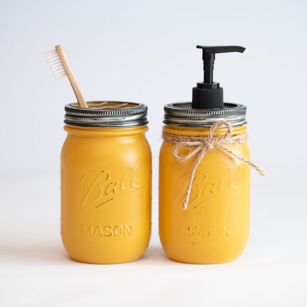 Two yellow mason jars with a toothbrush and pump dispenser on a white background.
