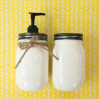 Two white mason jars with black lids on a yellow and white chevron patterned background.