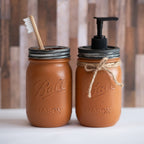Two mason jars, one with a toothbrush and the other with a pump dispenser, on a wooden surface.