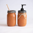 Two mason jars, one with a straw and the other with a pump dispenser, on a light background.