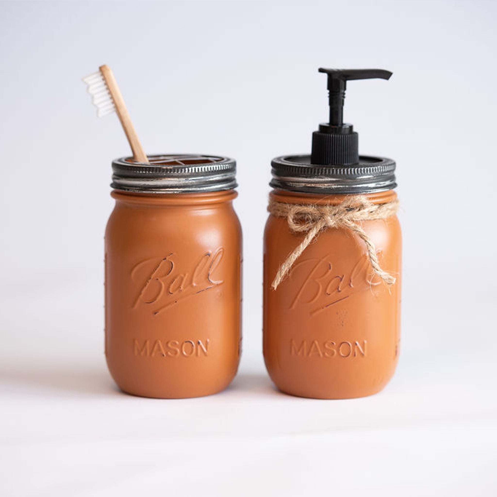 Two mason jars, one with a straw and the other with a pump dispenser, on a light background.