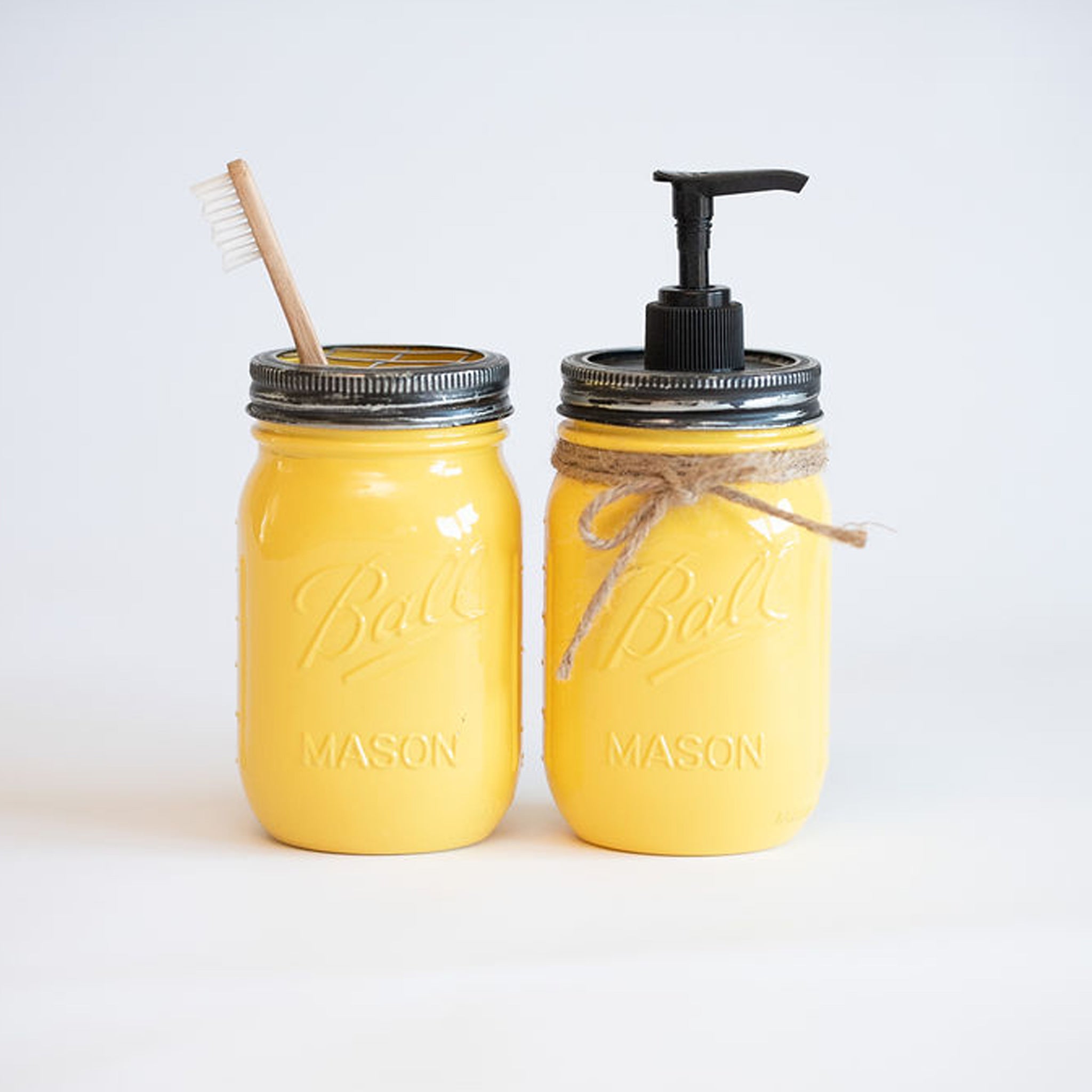 Two yellow mason jars with a straw and pump on a white background.