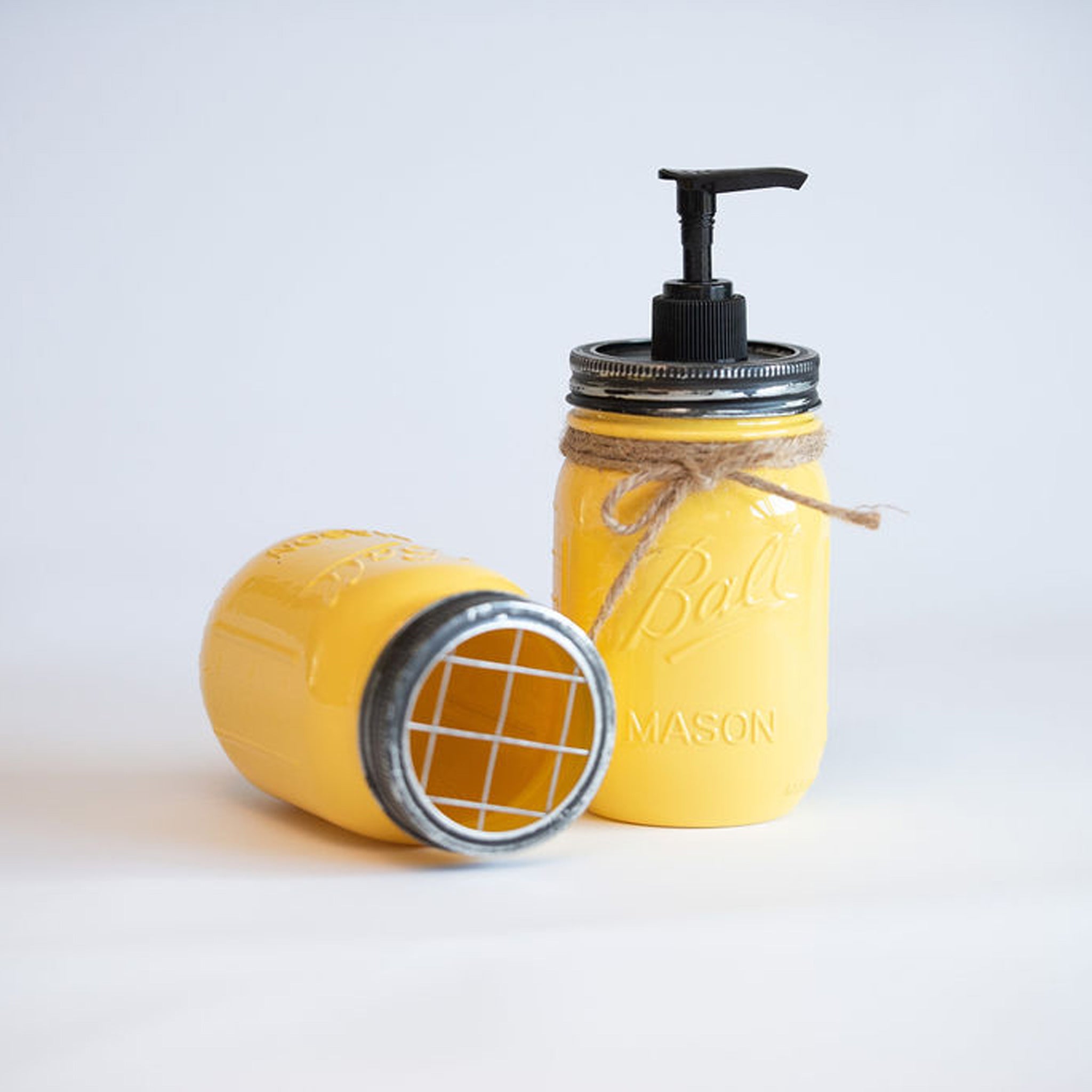 Yellow mason jar soap dispenser with pump on a light gray background.