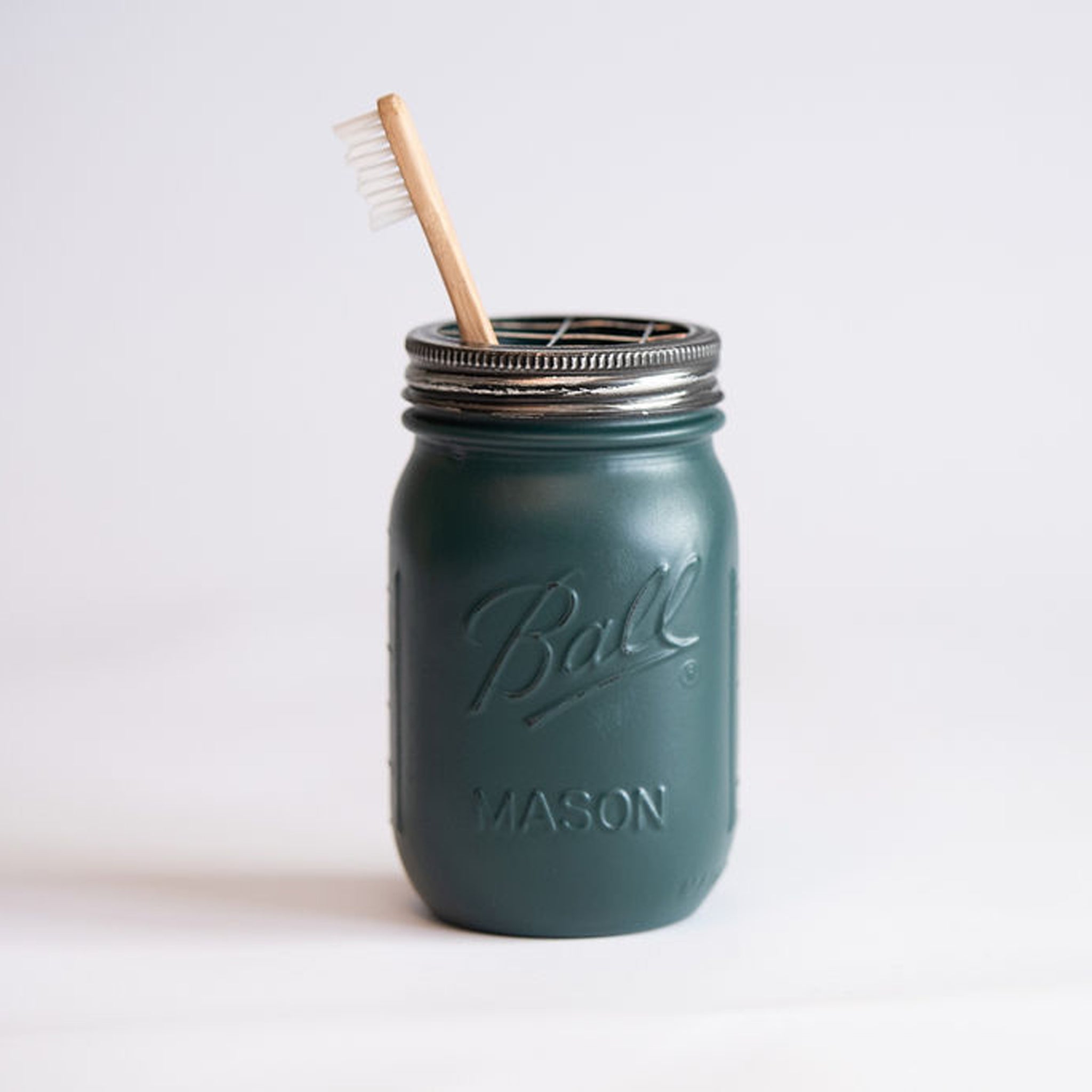 A Atlantic Green mason jar with a metal lid and wooden toothbrush on a light background.