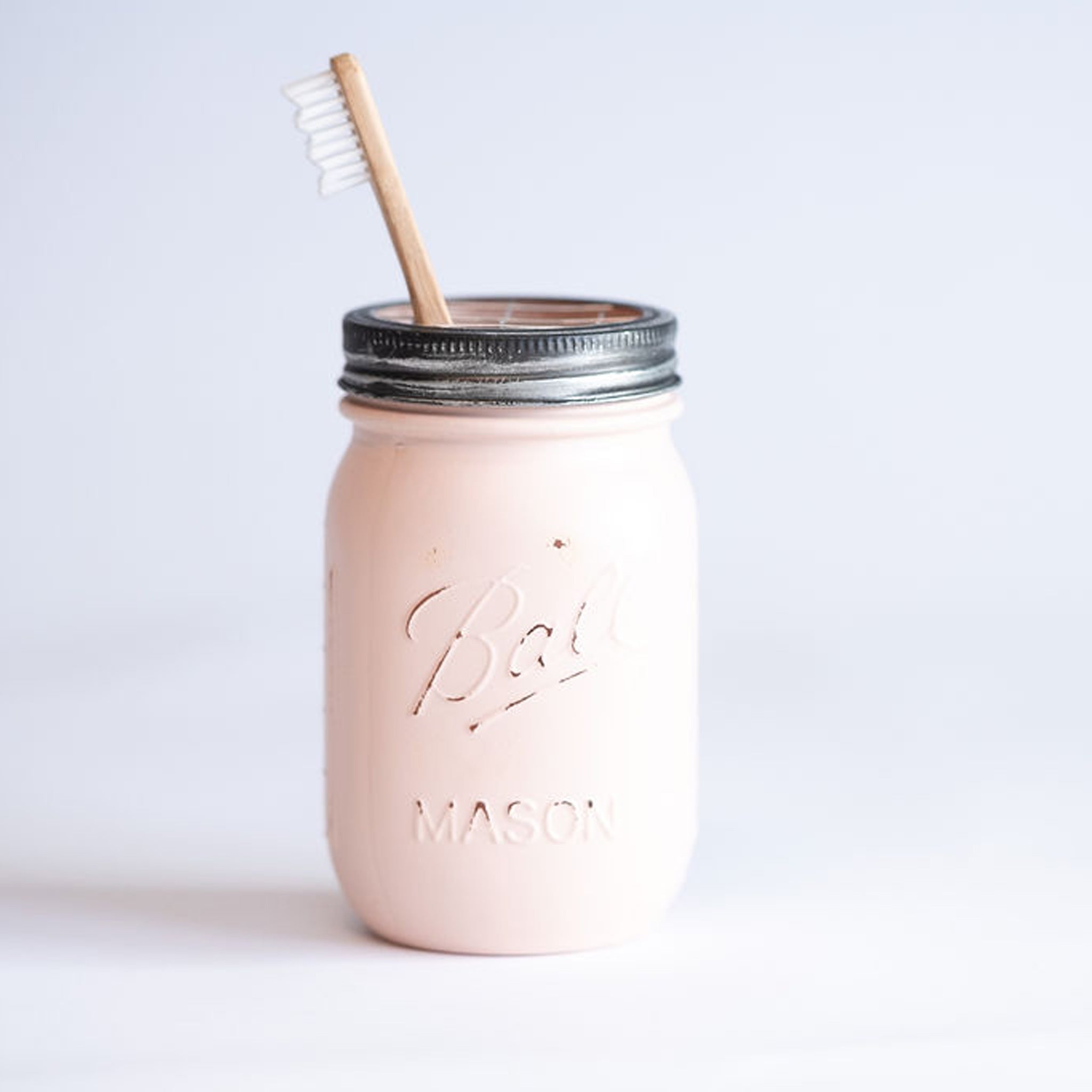 A white mason jar with a lid and a toothbrush on a light background.