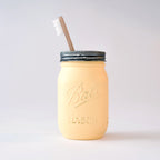 A yellow mason jar with a wood toothbrush in it on a white background.