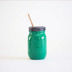 A green mason jar with a toothbrush in it  on a white background.