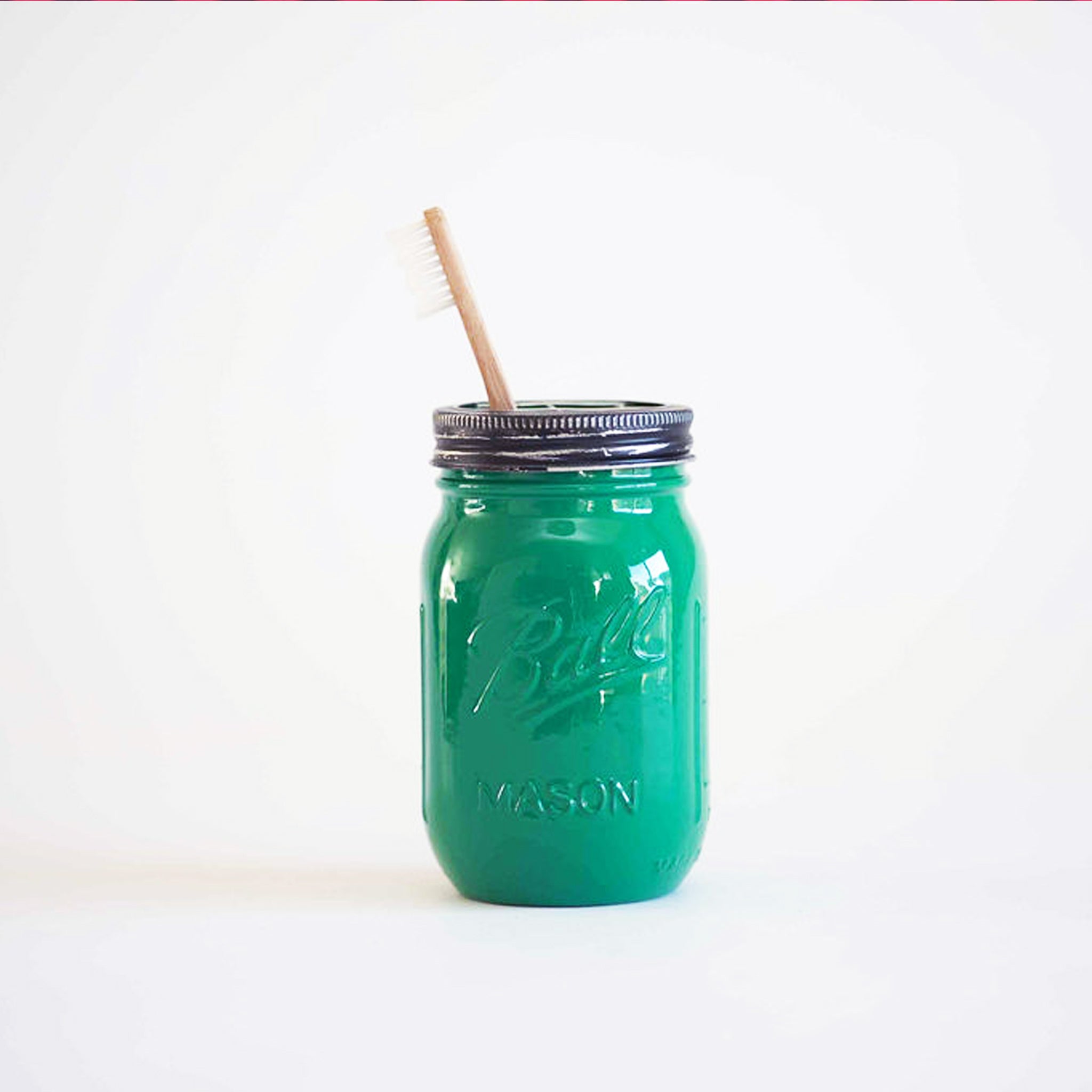 A green mason jar with a toothbrush in it  on a white background.