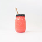 A coral mason jar with a metal lid and wooden toothbrush on a white background.