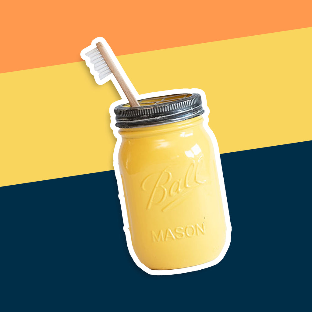 Yellow mason jar toothbrush holder on a multicolored background.