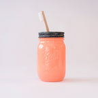 A coral mason jar with metal lid and toothbrush in it on a white background.